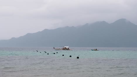 Barcos-Locales-De-Pesca-Y-Transporte-Que-Viajan-En-La-Bahía-De-Coron-Con-Una-Remota-Isla-Tropical-En-La-Distancia,-Palawan,-Filipinas,-El-Sudeste-De-Asia