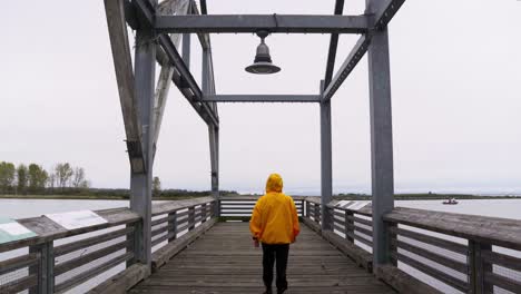 Wide-Shot-of-a-person-in-a-yellow-jacket-walks-down-into-a-dock-overlooking-water