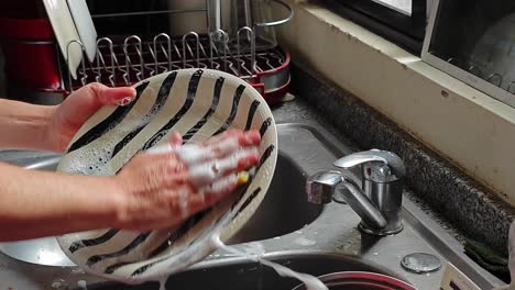 Mann-Wäscht-Das-Geschirr-Mit-Dem-Reinigungsschwamm,-Während-Er-Videos-Auf-Einem-Tablet-Ansieht