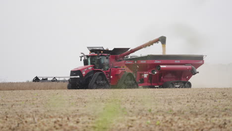 Combine-Harvester-Transferring-Grain-to-Bin-Pulled-by-Tractor-on-a-Dusty-Farm-Field
