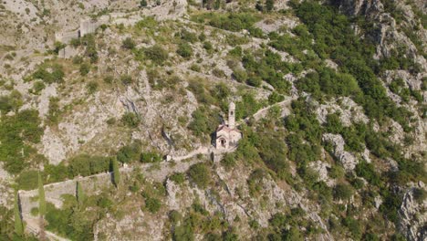 Aerial:-Church-of-Our-Lady-of-Remedy-in-Kotor,-Montenegro's-rugged-terrain