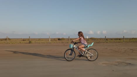 Long-red-hair-girl-riding-a-bike-in-street-a-sunny-desert-countryside