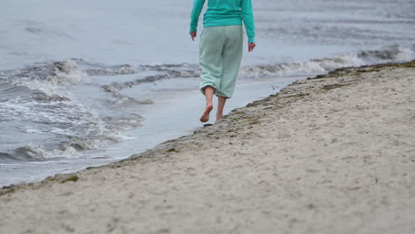 Person-walking-barefoot-on-the-sandy-beach,-waves-lapping-at-the-shore