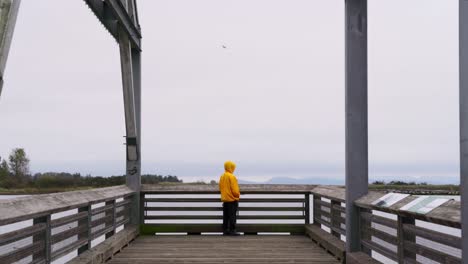 Mittlere-Aufnahme-Einer-Person-In-Einer-Gelben-Jacke,-Die-Am-Hafen-Steht-Und-Das-Wasser-überblickt