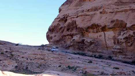 Tourism-adventure-tour-truck-driving-through-rugged-mountainous-terrain-of-desert-landscape-near-Petra-City-in-Jordan,-Middle-East