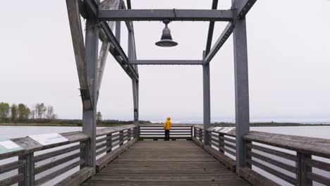 Wide-Shot-of-a-person-in-a-yellow-jacket-standing-dockside-overlooking-a-pier-of-fishing-boats