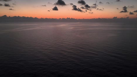 Drone-flying-backwards-during-beautiful-orange-sunrise-over-calm-sea