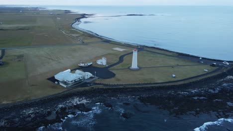 Drone-flying-away-from-a-tall-lighthouse-on-the-Icelandic-coast-and-over-a-beautiful-black-beach