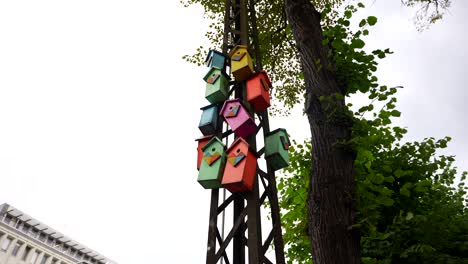 Low-angle-shot,-a-row-of-colorful-wooden-birdhouses-suspended-on-a-pole-along-the-street