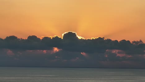 Orange-sun-bursting-through-clouds-during-beautiful-sunrise-over-calm-sea