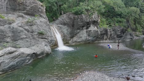 Drone-flight-over-lake-and-waterfall-with-swimming-tourist-in-Bani,-Dominican-Republic---approaching-shot