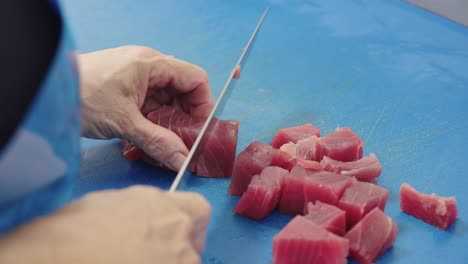 Fishmonger-cutting-bluefin-tuna-cubes-for-cooking-on-blue-surface