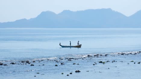 Group-of-local-Timorese-fishermen-in-small-wooden-boat-bringing-in-fishing-nets-along-the-coastline-of-ocean-in-Dili,-Timor-Leste,-Southeast-Asia