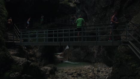 Push-in-to-tourists-enjoying-gorge-views-of-deep-canyon-walls-of-Almbachklamm-from-metal-bridge