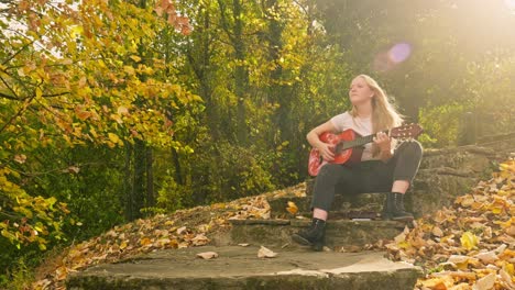 Herbst-Goldene-Blätter-Herbst-Blondes-Mädchen-Klimpert-Gitarre-Sunburst-Lichtstrahl