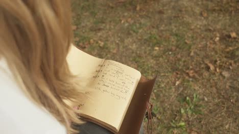 Over-shoulder-shot-young-blonde-woman-writes-poetic-lyrics-in-book