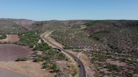 Carretera-Con-Dos-Autos-Al-Frente-Filmada-Con-Un-Dron-Y-Montañas-Al-Fondo