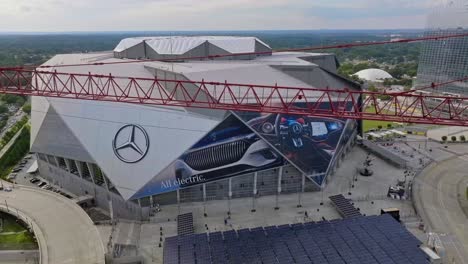 Aerial-orbit-shot-of-Mercedes-Benz-Stadium-and-red-industrial-crane-with-waving-american-flag-in-foreground