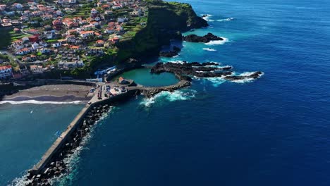 Aerial-of-Seixal-Natural-Pools,-blue-sea,-beach-and-town-in-Madeira