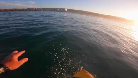 POV-Of-A-Surfer-Standing-And-Balancing-On-A-Board,-catching-some-waves,-surf-Foiling-In-The-Sea-at-sunrise-in-caparica-beach