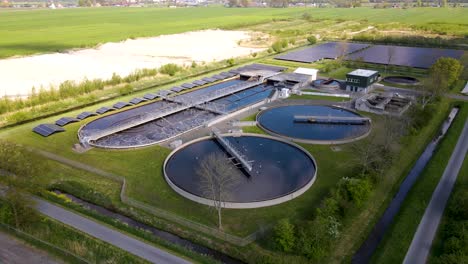 Panoramic-aerial-shot-of-a-large-water-treatment-plant-with-agitation-tanks-and-aeration-chamber-located-on-a-grassy-countryside-landscape