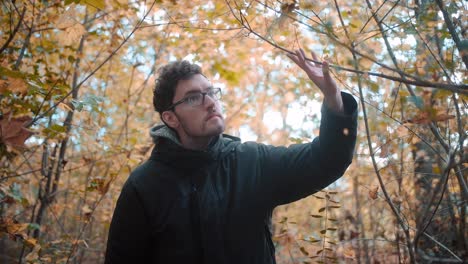 Immersive-slow-motion-of-a-young-European-male,-adorned-with-a-beard-and-glasses,-attentively-navigating-the-underbrush-of-a-mixed-forest-during-the-vibrant-autumn-season-in-Germany