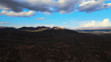 Drone-shot-flying-over-hills-in-Salta,-Argentina-towards-dramatically-lit-mountains