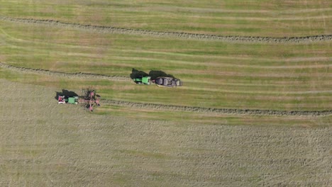 Top-down-aerial-view,-tractor-with-hay-tedder-creates-row-to-produce-silo-bales