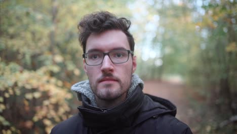 In-captivating-slow-motion,-a-young-European-man-with-sharp-glasses-and-a-stylish-beard-finds-solace-in-an-autumnal-mixed-forest,-his-gaze-piercing-the-distant-horizon,-lost-in-thought