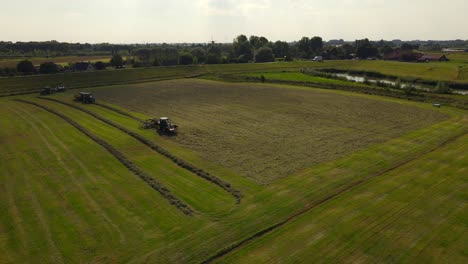 Tractor-makes-rows-of-grass-to-pack-them-into-silo-bales,-aerial-orbit-sunset