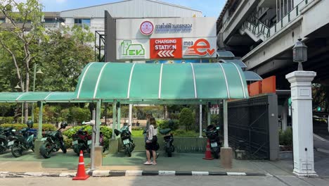 View-of-the-signage-board-of-the-electric-car-charging-station-and-people-walking-in-downtown-Bangkok,-Thailand