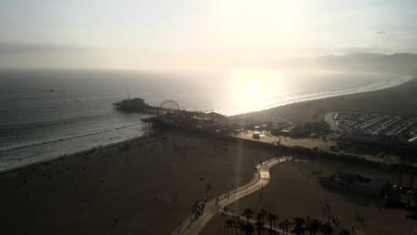 A-scenic-view-of-the-Santa-Monica-amusement-park-at-sunset,-with-ocean-waves-lapping-at-the-shoreline