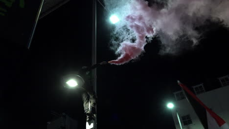 A-masked-protester-sets-off-a-red-smoke-flare-after-climbing-up-a-lamppost-during-a-pro-Palestinian-protest-outside-the-Israeli-embassy-at-night