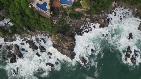 Houses-with-pools-on-cliffs,-waves-crashing-against-rocks-in-Puerto-Escondido,-Oaxaca