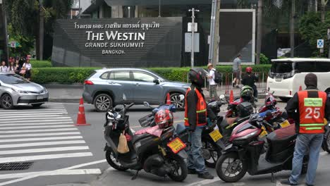 Busy-sights-of-traffic,-motorcycle-taxi-drivers-chit-chatting-and-people-walking-outside-the-Five-star-hotel,-The-Westin-Grande-Sukhumvit-Bangkok,-Thailand