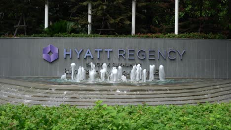 Frontal-view-with-water-fountain-against-the-display-sign-of-the-Five-star-hotel-Hyatt-Regency-located-in-the-heart-of-Sukhumvit-with-direct-access-to-BTS-Skytrain-Nana-station,-Bangkok,-Thailand