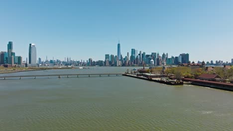 Aerial-establishing-drone-shot-of-Manhattan-Skyline-with-One-World-Trade-Center-and-bridge-connecting-to-Ellis-Island-in-foreground---New-York-City-in-summer-season