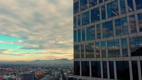 Drone-ascending-beside-reflection-of-cloudy-morning-sky-on-tall-building-windows-cityscape