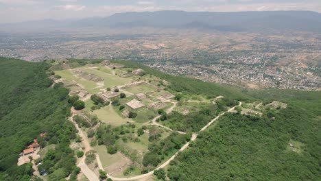 Aerial:-Monte-Albán-ruins-in-Oaxaca,-overlooking-a-vibrant-Mexican-city-landscape