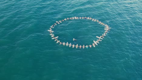 Aerial-view-of-dozens-of-people-floating-in-the-sea-at-Samara-beach-carrying-surfboards-in-a-circle-formation