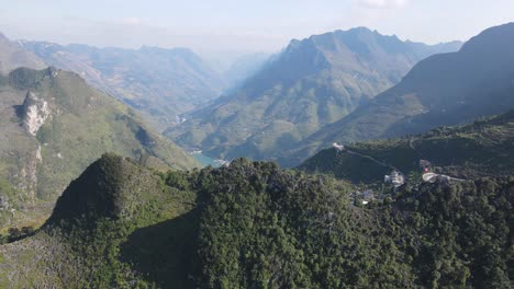 Drohnenbewegungen-über-Einem-Felsigen-Berggipfel-Offenbaren-Ein-Kleines-Dorf-Und-Einen-Grünen-Nho-Que-Fluss-Im-Hintergrund,-Ha-Giang-Vietnam