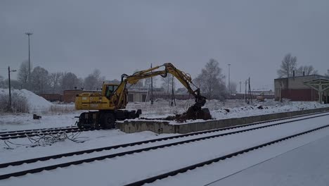 Railroad-excavator-digging-and-moving-dirt-along-railroad-in-snow-blizzard