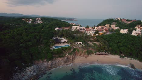 Sunset-over-Huatulco,-Mexico-with-coastal-homes-and-dense-greenery---Aerial