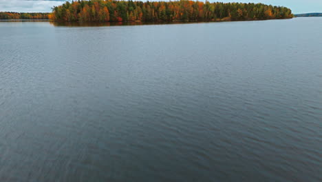 In-Nahaufnahme-über-Das-Wasser-Eines-Sees-Rasend,-Sich-Nach-Oben-Neigend,-Offenbart-Sich-Ein-Inselarchipel-Mit-Einem-Herbstlichen-Wald-Aus-Roten,-Grünen,-Gelben-Und-Braunen-Bäumen-In-Valkeakoski,-Finnland