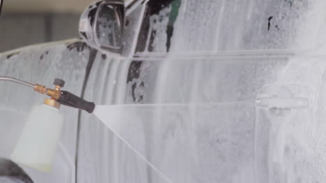 Close-up-of-car-wash-foam-gun-spraying-white-foam-on-car-window