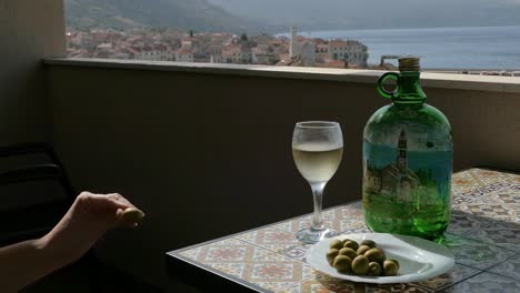 Woman-enjoying-green-olives-with-wine-on-terrace-in-seaside-town