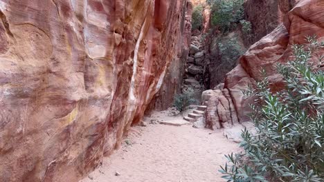 Walking-along-a-path-in-Petra,-Jordan-to-find-ancient-stairs-carved-in-the-sandstone