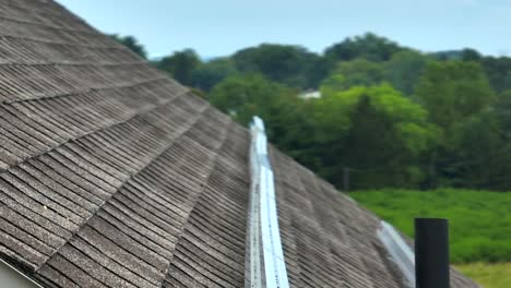 Close-up-of-a-solar-rail-on-a-shingled-roof,-with-a-backdrop-of-lush-greenery-in-America