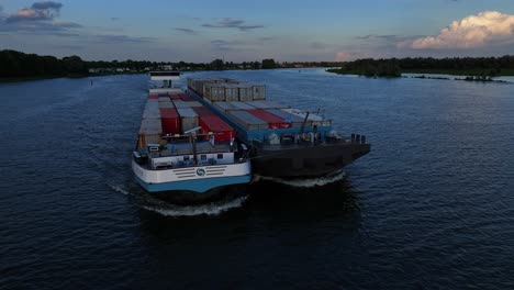 Low-flying-drone-view-of-cargo-ships-with-containers-sailing-together-on-Dutch-rivers-delivering-cargo