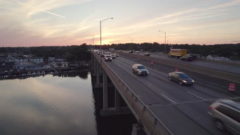 Drone-Shot-Tracking-Forward-Next-to-Interstate-on-Bridge-at-Sunset,-with-Light-Traffic-Flow